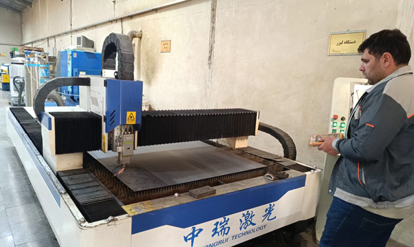 یکی از تکنسینهای کارگاه تابلو برق آراد مهر در حال برش ورق با دستگاه لیزر